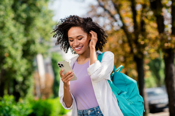 照片的梦幻闪亮的女士穿着白色衬衫帆布背包享受阳光明媚的天气写短信现代设备外的城市公园图片下载