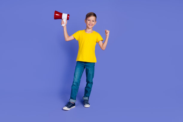 照片中，风趣开朗的小男孩穿着时髦的衣服，拿着扩音器举起拳头，孤立在紫色的背景上图片下载