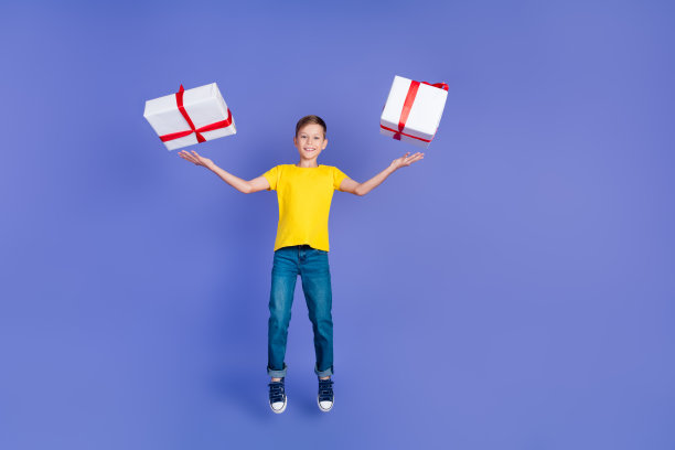 照片积极开朗可爱的好男孩穿着时髦的黄色衣服抓住两个礼品销售折扣孤立在紫色的背景图片下载