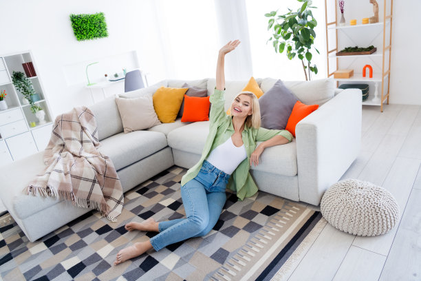 迷人的年轻女子的全身照片坐地板舒适的周末休息穿着时尚的绿色衣服生活区明亮的室内设计图片下载