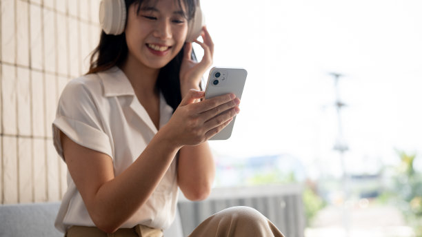 照片中，一名女子戴着耳机听音乐，一边使用智能手机。图片下载