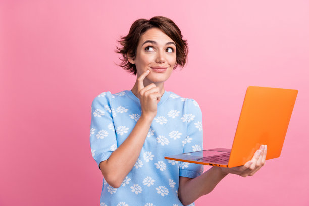 聪明的创意女士的照片，手指触摸下巴，拿着笔记本电脑，在粉红色的背景上看起来空空荡荡图片下载