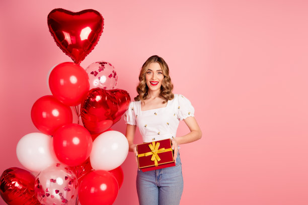 可爱的年轻女子的照片肖像，气球抱着礼物，穿着时尚的白色衣服，发型孤立在粉红色的背景上图片下载