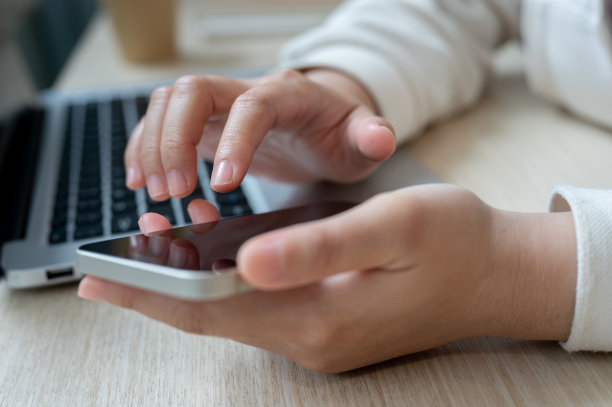 一个女人在工作时触摸她的智能手机屏幕，查看信息的特写照片。图片下载
