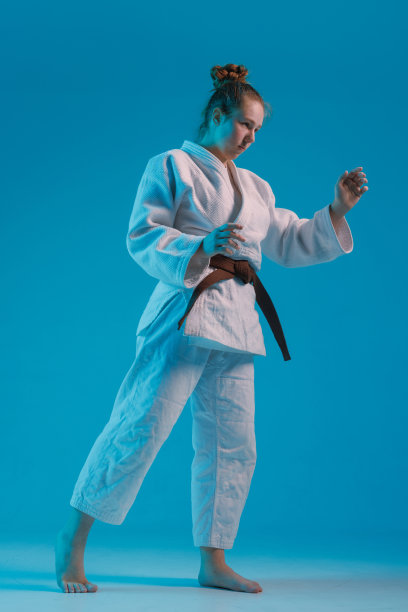 女孩柔道在白色和服与黑腰带在蓝色背景，工作室照片图片下载