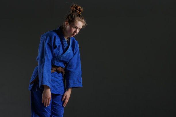 女孩柔道在白色和服与黑腰带在蓝色背景，工作室照片图片下载