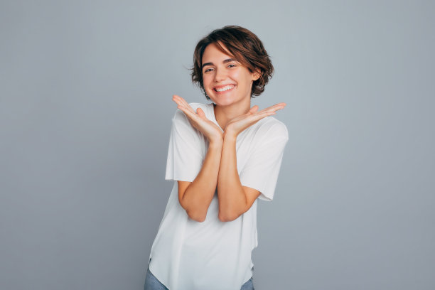 迷人的微笑年轻女性与健康的皮肤和现代的发型在一个灰色的墙背景下摆出好心情的照片图片下载