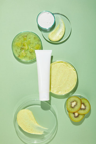 猕猴桃去角质霜主题广告照片，各种尺寸的圆形玻璃底座平放在绿色的桌面上，中间有一个白色的管子。照片是从高角度拍摄的，复制空间图片下载