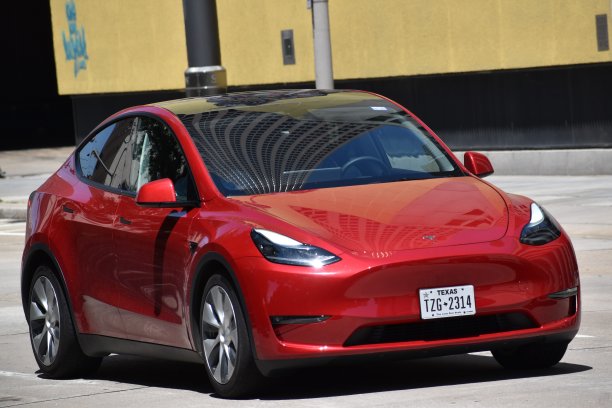 一辆红色特斯拉电动汽车在市中心行驶的肖像图片下载