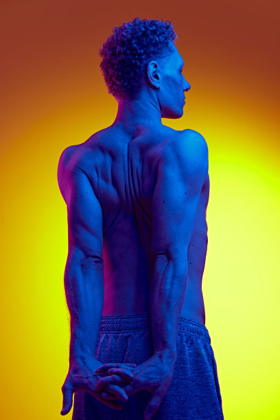 光着膀子的男子的后视图，在蓝色霓虹灯的黄色背景下，强壮的背部摆姿势。肌肉的身体图片下载