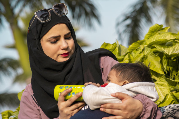 年轻的穆斯林母亲在户外用奶瓶喂婴儿的照片。图片下载