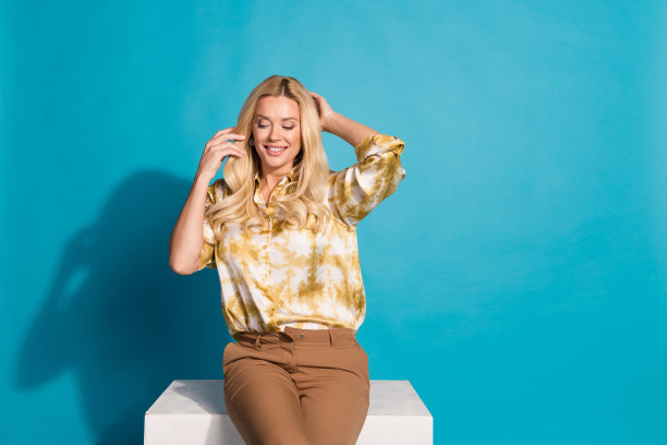 照片肖像迷人的成熟女子坐在立方体丝绸般的头发触摸穿着时尚的正装衣服孤立的青色背景图片下载