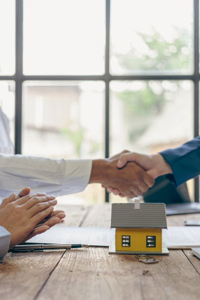 房屋销售代表握手，祝贺客户成功获得房屋贷款。桌子上有一份合同文件，上面有房子的平面图。特写照片图片下载