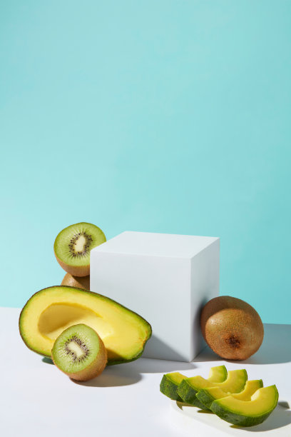 矩形的空白讲台放置在淡蓝色背景的中心，周围装饰着新鲜的鳄梨和猕猴桃。照片从正面拍摄，为宣传腾出空间图片下载