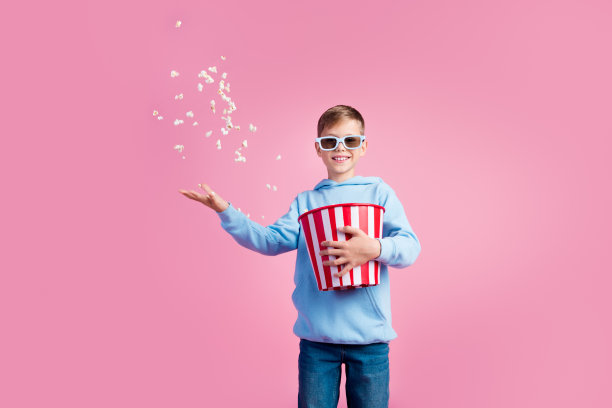 照片积极的小男孩看电影3d眼镜手臂持有扔爆米花空空间孤立的粉红色背景图片下载