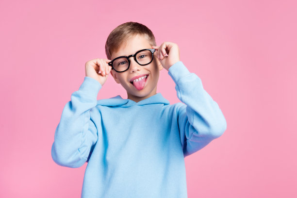 积极的小学生的照片显示舌头伸出手臂触摸眼镜空白空间孤立在粉红色的背景图片下载