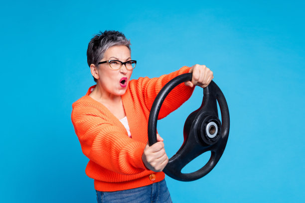 可爱的高级女士的照片肖像拿着方向盘烦恼穿着时尚的橙色服装孤立在蓝色背景图片下载