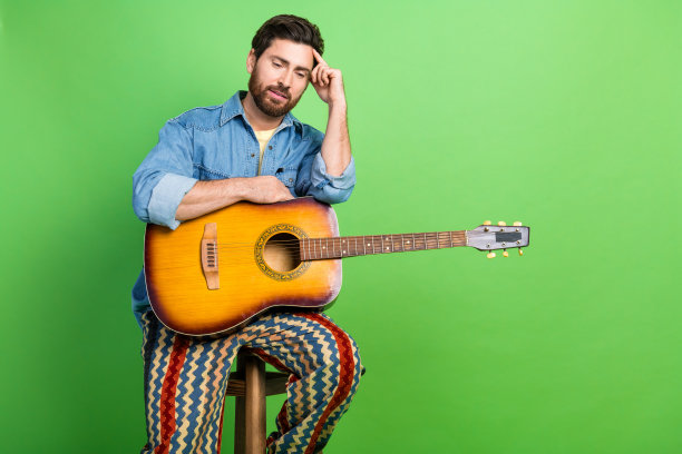 照片中梦幻般的帅哥穿着牛仔夹克享受吉他音乐空旷的空间孤立的绿色背景图片下载