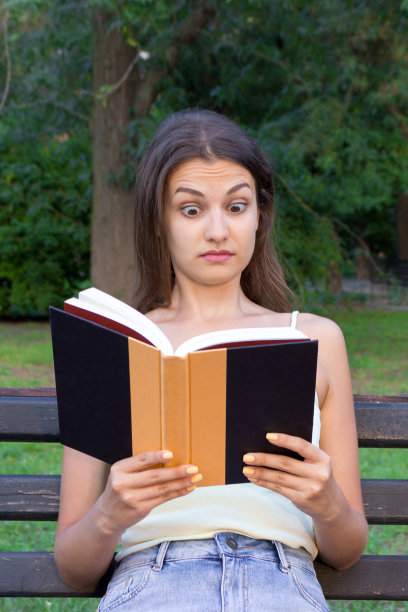 惊讶，困惑，睁大眼睛的女人正在公园的长凳上看书图片下载