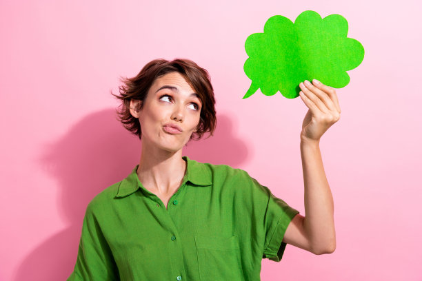 漂亮的年轻女孩的照片肖像持有怀疑的漫画纸云穿时髦的绿色服装孤立在粉红色的背景图片下载