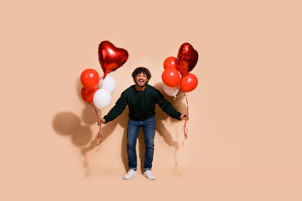 印象深刻的正面男子穿着运动衫拿着气球空空间孤立米色背景的全长照片图片下载