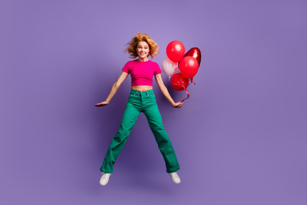 照片正面可爱的女人穿着时髦的粉红色衣服，有有趣的氦气球孤立在紫色的背景图片下载
