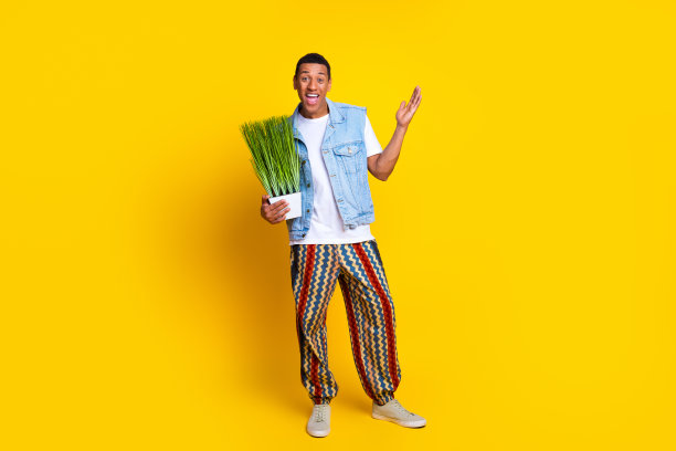 全尺寸照片，印象深刻的男人穿着牛仔背心，t恤，抱着植物手臂，惊讶地盯着孤立的黄色背景图片下载