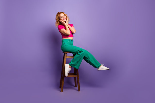 照片可爱可爱的开朗的女人穿着时尚的粉红色衣服，坐在木椅美容沙龙孤立的紫色背景图片下载