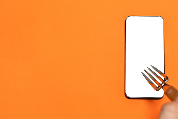 拿着叉子的手拿着黑屏手机。橙色背景。网上食品购物。带有复制空间的图像。图片下载