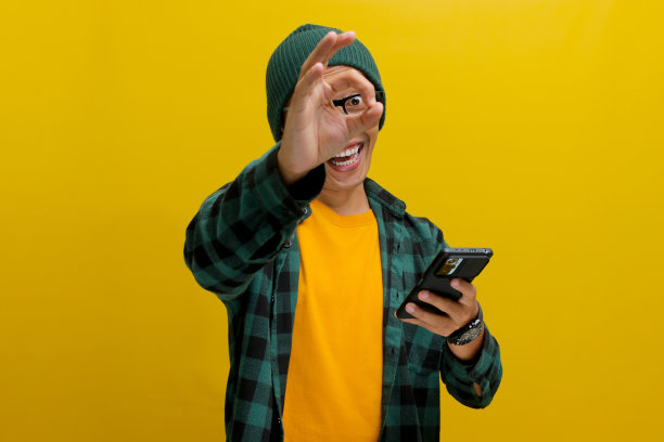 一名亚洲男子拿着智能手机做了一个OK的手势图片下载