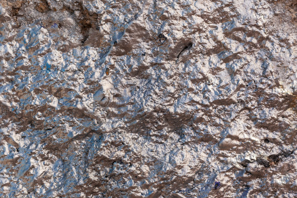 粗糙而皱巴巴的混凝土墙被涂上了玫瑰银色的闪亮油漆。水平的照片图片下载