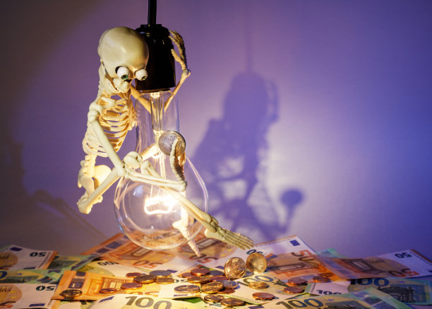 在紫色的背景下，一个有趣而快乐的骷髅在灯泡上摇摆，宣传节约用电。文本的自由空间。水平的照片图片下载