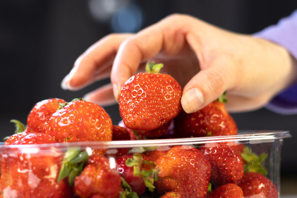 一名妇女从包装中取出新鲜的红草莓。关闭了。图片下载
