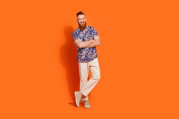全长照片乐观的好满意的家伙穿印花衬衫裤子站手掌折叠孤立的橙色背景图片下载