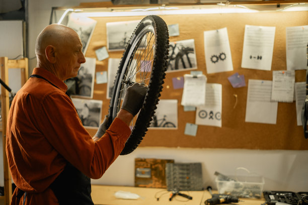 老男工人拿着自行车车轮修理自行车。自行车车间内部。图片下载