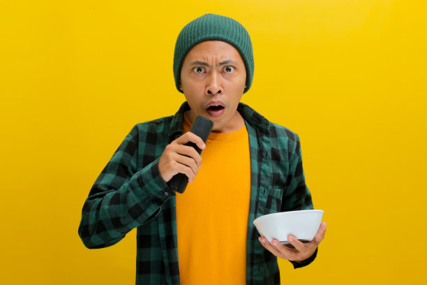 惊讶的年轻亚洲男子暂停了视频，他拿着白色的碗，孤立在黄色的背景下图片下载