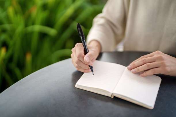 在这张特写照片中，一位亚洲女性坐在自家后院的一张桌子旁，享受着早晨在记事本上写字的放松和个人时间。图片下载