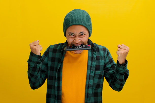 亚洲男人在看电视时感到愤怒和沮丧，沮丧地咬电视遥控器图片下载