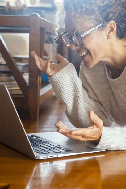 在舒适的工作场所，愉快而兴奋的女人赤脚躺在家里的地板上进行在线视频通话。享受电脑视频通话连接的女性。用手打手势图片下载