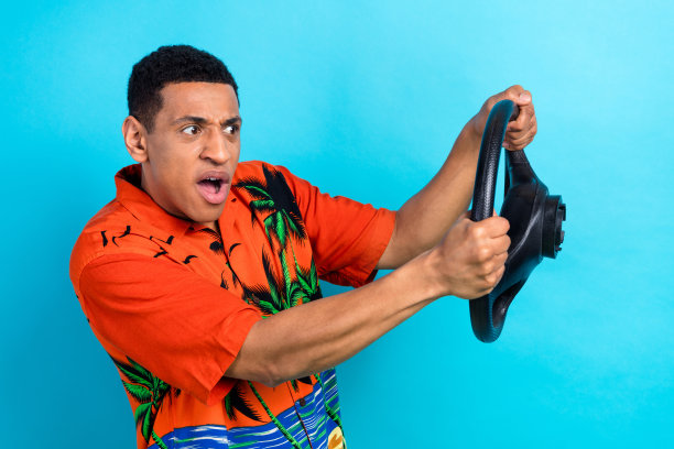 印象深刻的震惊男子穿着印花衬衫驾驶汽车孤立的蓝色背景的照片图片下载