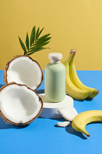 蓝色桌子上的圆形底座上放着一瓶绿色的空白有机化妆品，周围摆放着香蕉和椰子。黄色背景上的前视图照片，用于添加文本的空间图片下载