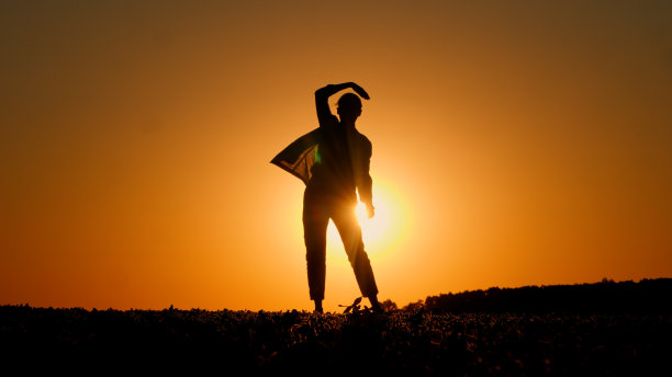 日落时分，一位年轻的火辣辣的女子在田野里热情地跳舞，背景是橙色的天空。图片下载