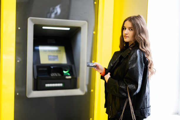 年轻的黑发女孩在黄色自动取款机上从信用卡里取钱。图片下载