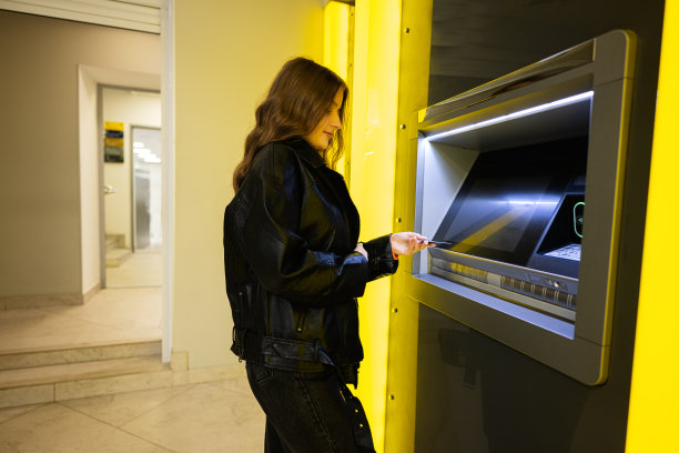 年轻的黑发女孩在黄色自动取款机上从信用卡里取钱。图片下载