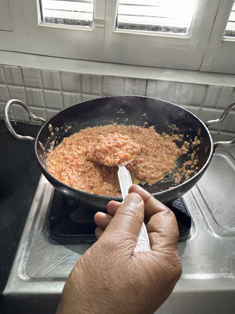 特写图片:无法辨认的人在卡拉希烹饪锅里搅拌胡萝卜哈瓦(哈瓦加加尔)，厨房柜台上的便携式燃气燃烧器，印度甜点，胡萝卜在水、牛奶和糖中煎炸，金属勺子，高架视图，重点放在前景图片下载