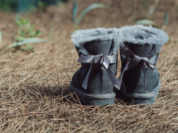 在棕色的森林地面上，孩子们灰色的羊皮靴子上有蝴蝶结的水平近景。图片下载