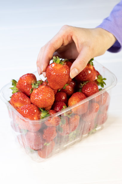 一名妇女从包装中取出新鲜的红草莓。关闭了。图片下载