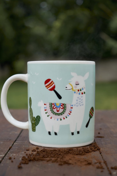 吸烟咖啡杯与秘鲁美洲驼设计。杯子被堆放在木桌上，你可以看到咖啡豆。咖啡杯是在外面与自然背景，垂直照片。图片下载