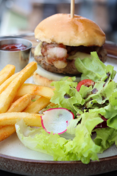 特写图片生菜、萝卜和番茄配菜沙拉配培根芝士汉堡白面包汉堡包，一堆脆脆的炸薯条，金属框架的番茄酱，重点在前景图片下载