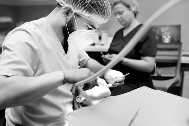 现代医疗中心的牙医和病人。医生在医院治疗年轻女子的牙齿。医生在正畸或修复治疗前检查病人。黑白照片图片下载
